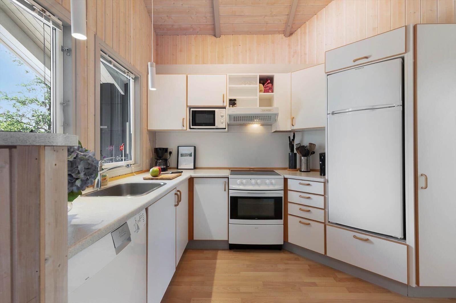 Küche mit weißen Schränken, Kühlschrank, Herd und Fenster.
