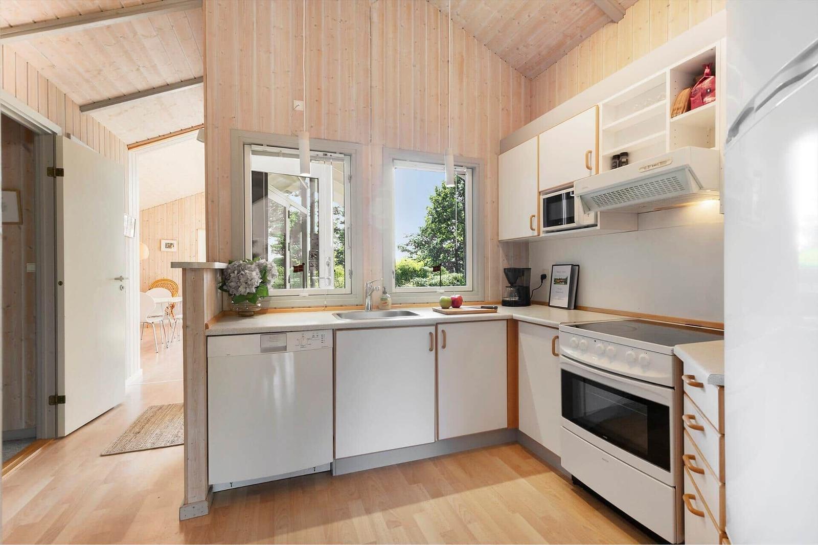 Küche mit weißen Schränken, Herd, Spüle und Fenster zum Garten.