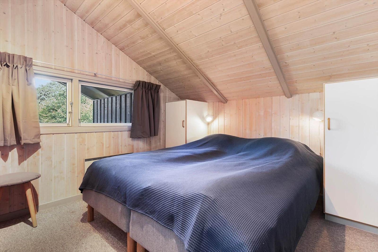 Schlafzimmer mit Holzwand, Bett und Fenster