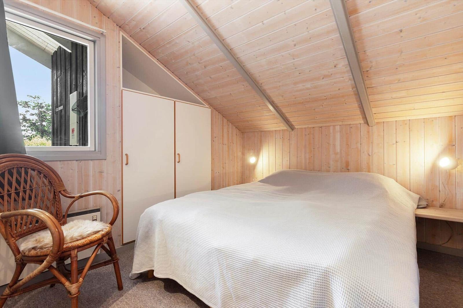 Schlafzimmer mit Holzwand, Bett, Stuhl und Fenster. Decke schräg.