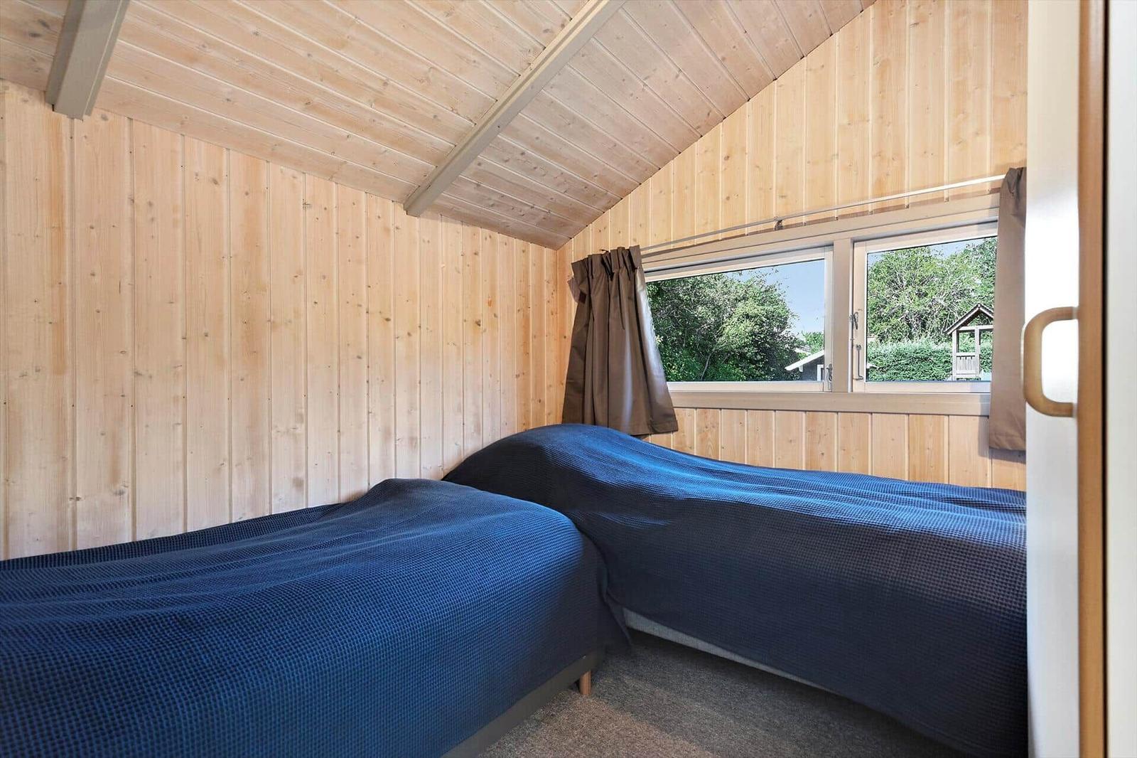 Zwei Betten mit blauen Bettdecken in einem Holzhaus mit Fenster.