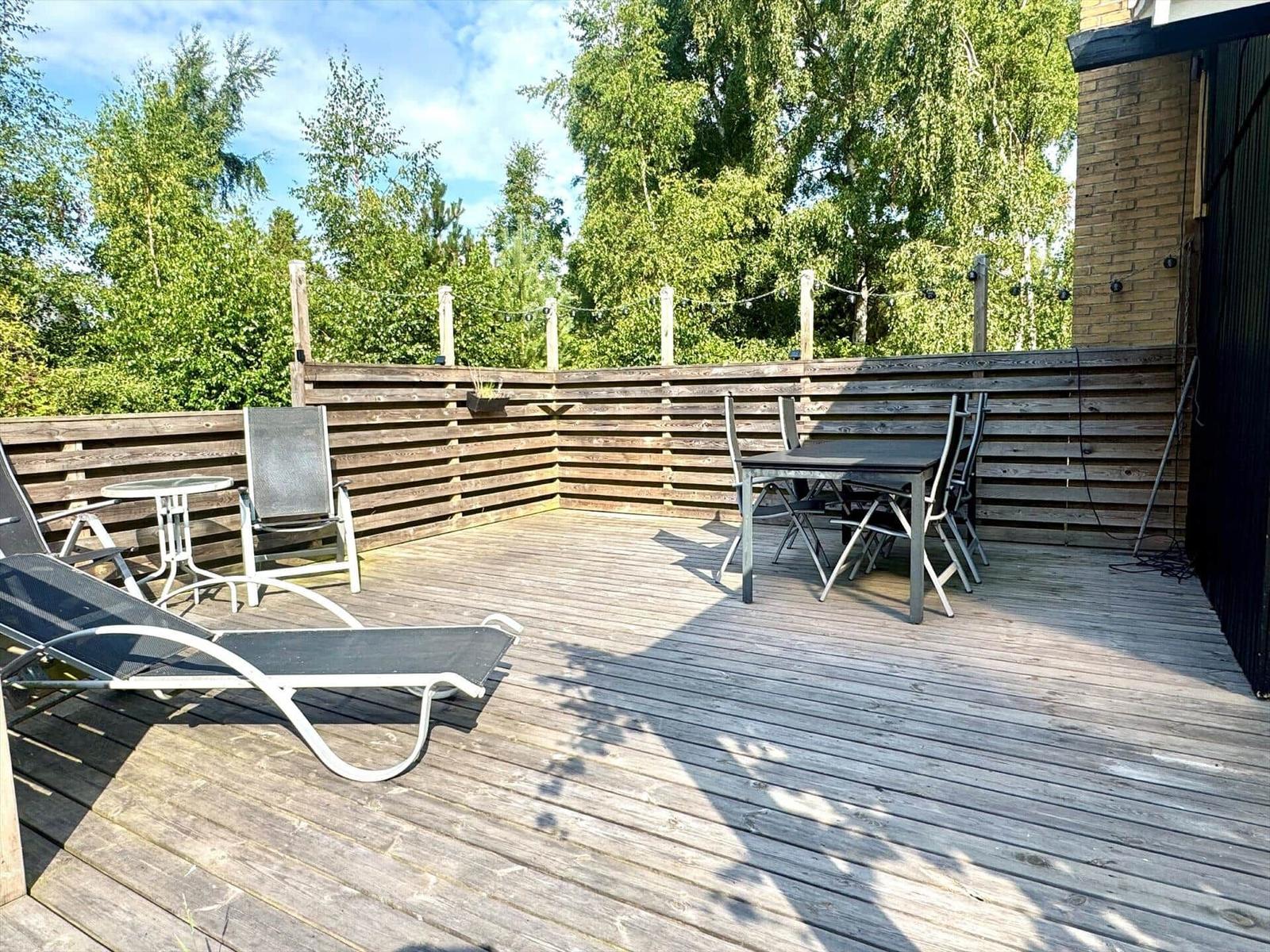 Deck with lounge chairs and table set, surrounded by wooden railing and trees.