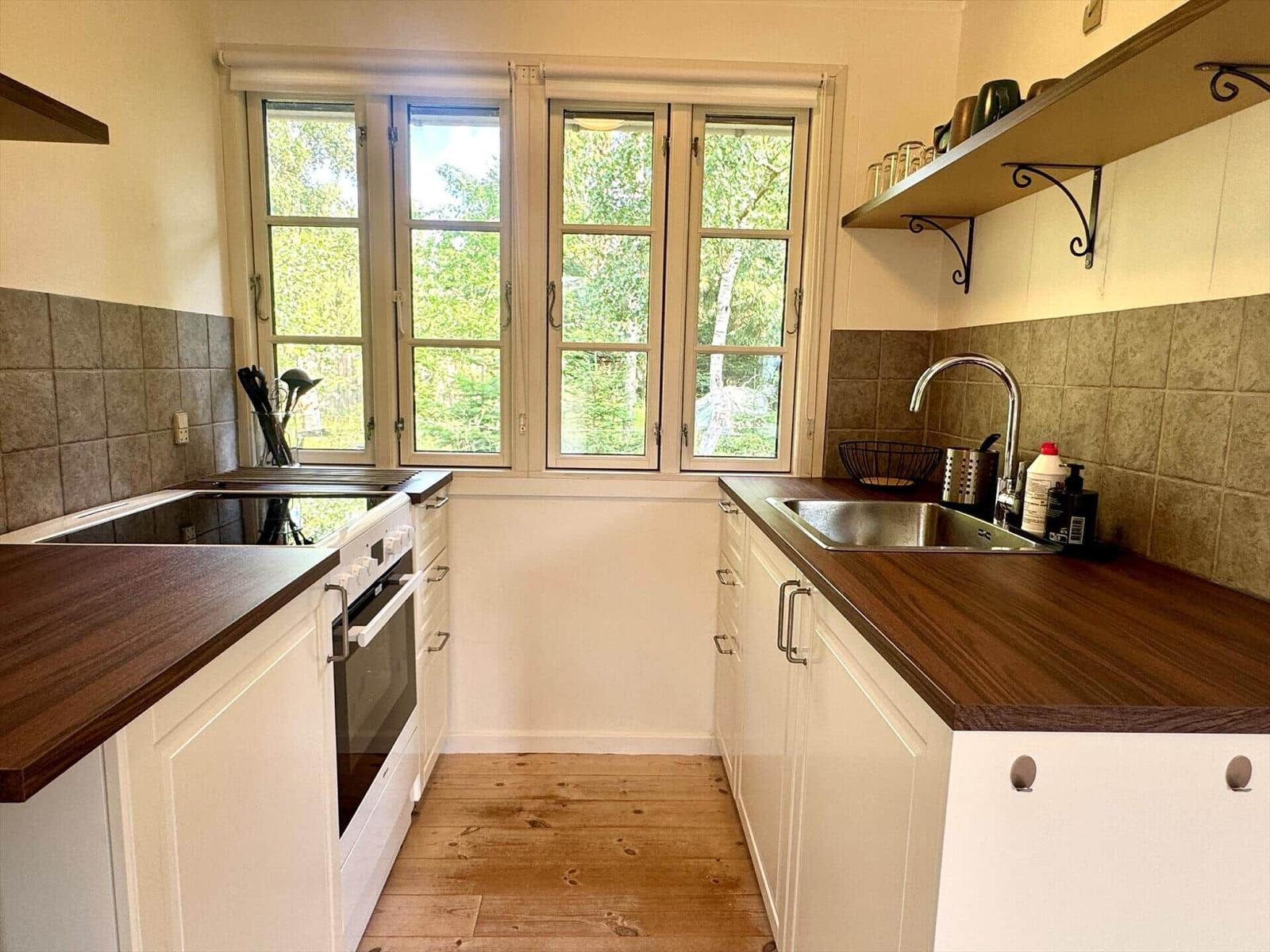 Kitchen with white cabinets, wooden countertops, and windows to the garden.