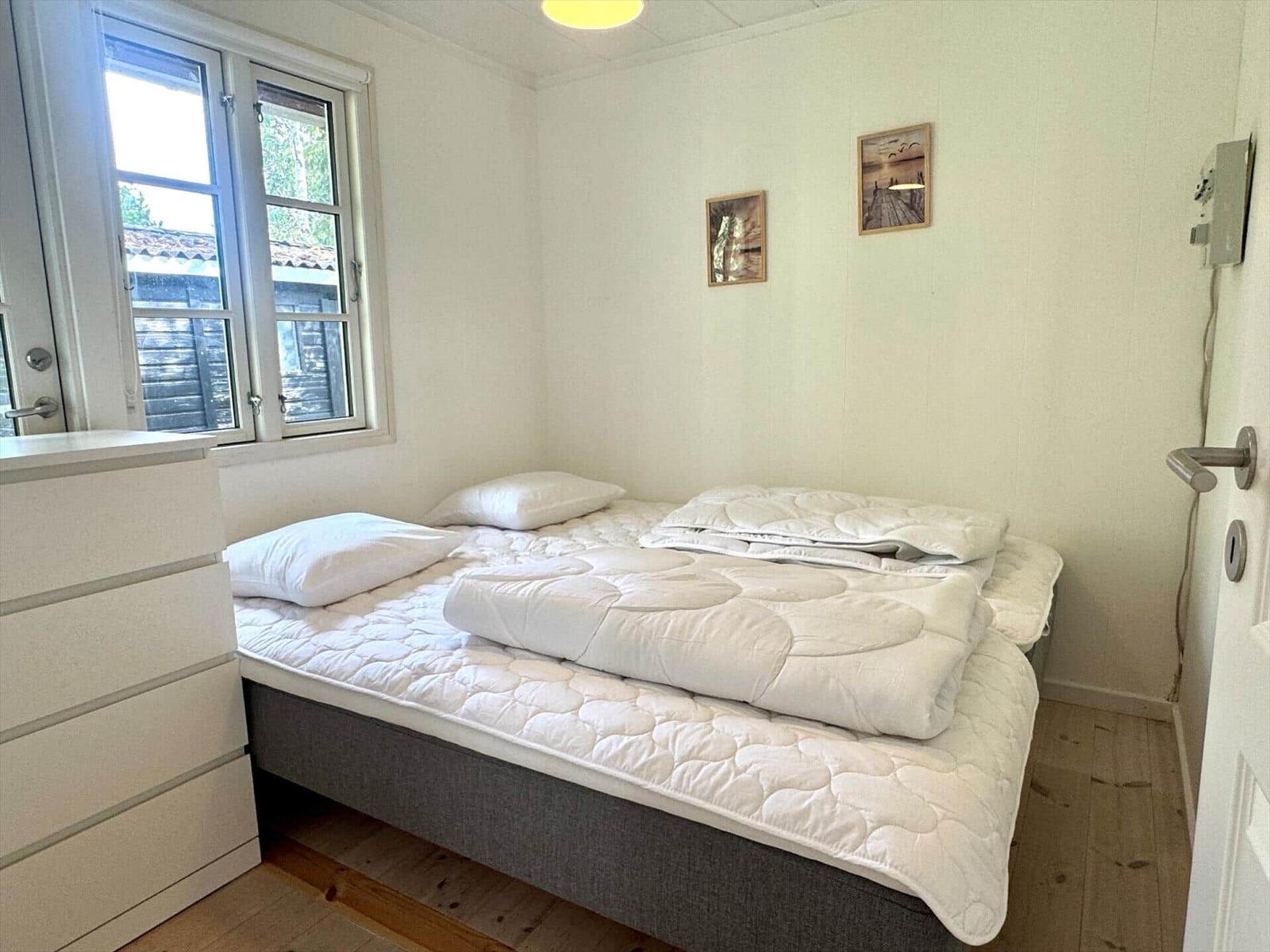 Bedroom with bed, window, and dresser. Wall pictures and wooden floor.