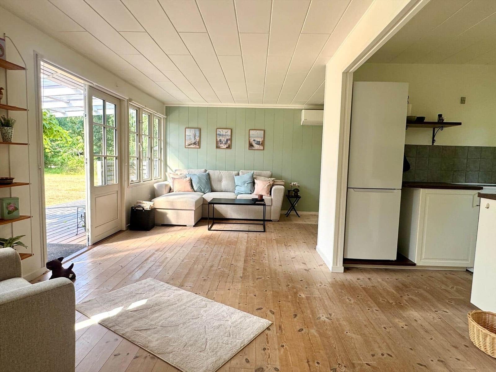 Living area with sofa, kitchen area, and terrace overlooking a green area.