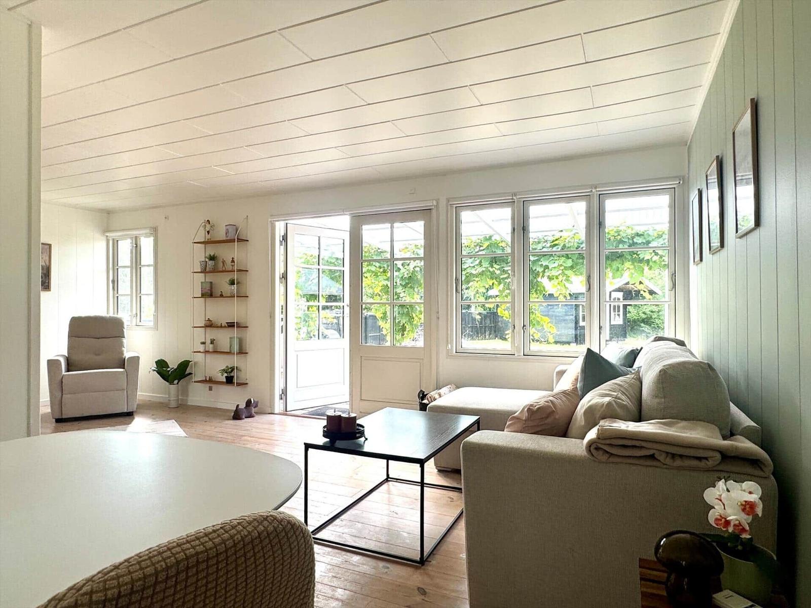 Living room with sofa, coffee table, and view of garden. Wooden floor and large windows.