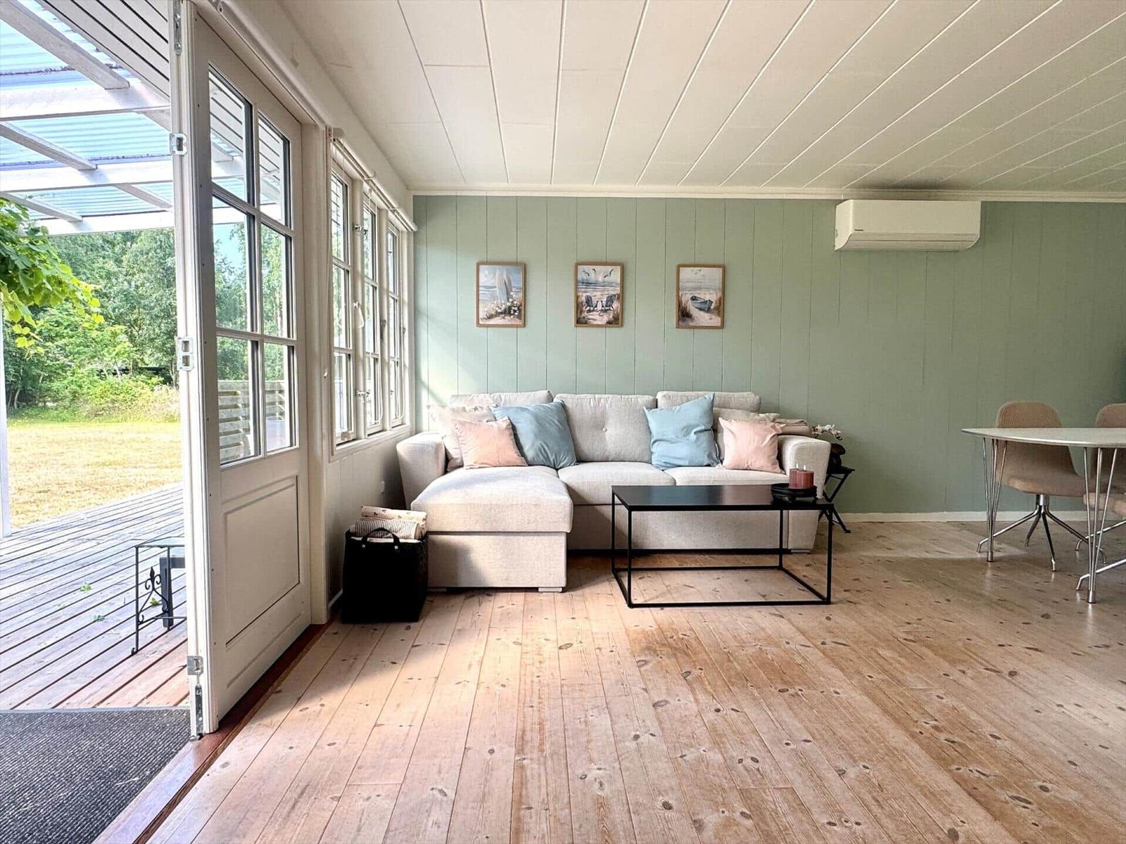 Living area with sofa, table, and windows. Wooden floor and green walls.