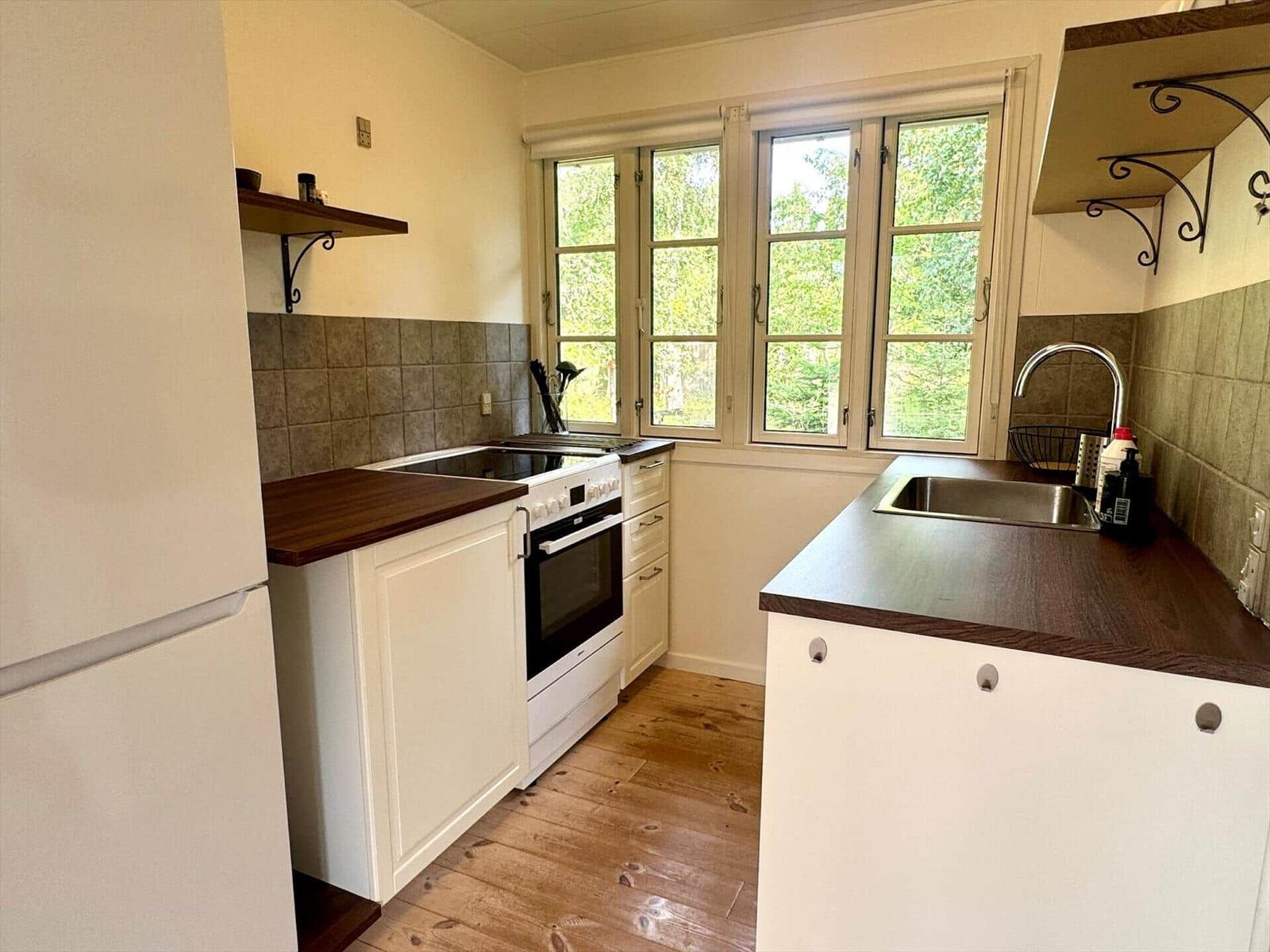 Kitchen with white cabinets, dark countertop, and wooden floor. Windows with view of greenery.