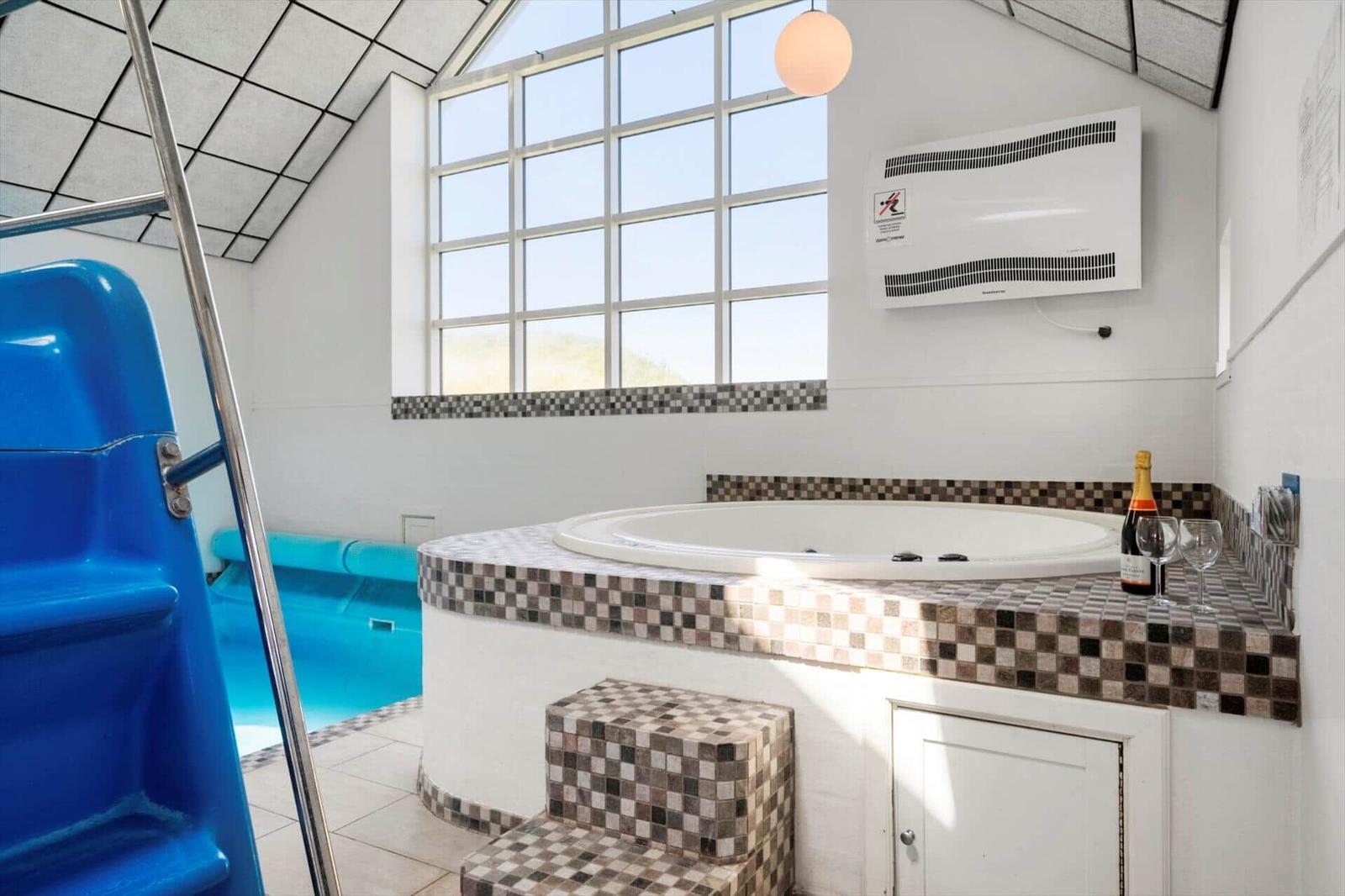Whirlpool mit Sitzbank und Blick auf Pool. Wandheizung und Fenster mit Sicht auf Landschaft.