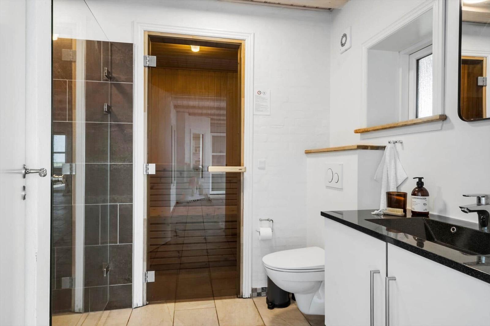 Badezimmer mit Dusche, Toilette und Sauna. Schwarze Arbeitsplatte und Spiegel.