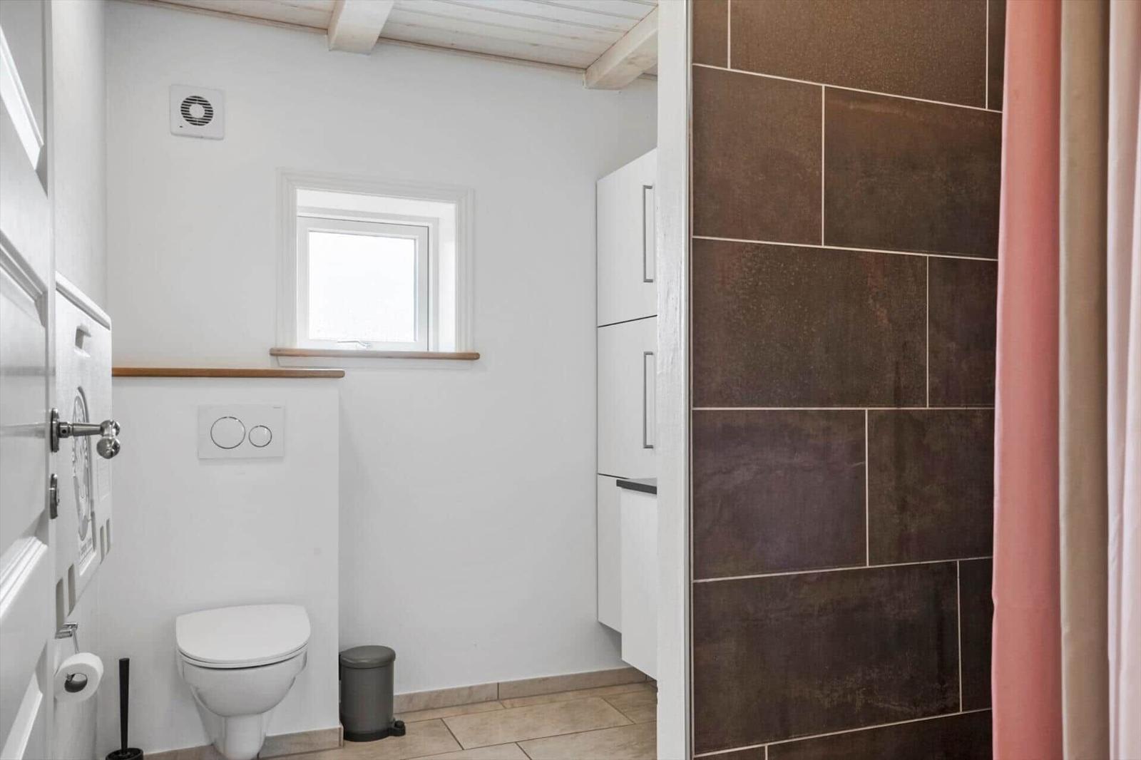 Badezimmer mit Toilette, Fenster und Dusche mit braunen Fliesen.