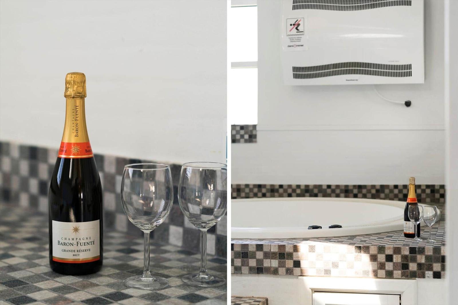 Badezimmer mit Whirlpool, Flasche Champagner und zwei Gläser auf Mosaik-Arbeitsfläche.