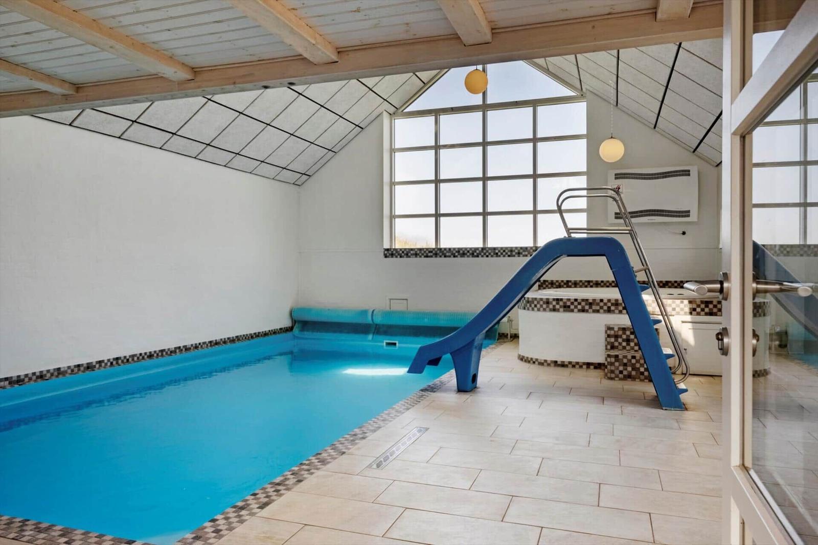Innere Schwimmhalle mit blauem Pool, Rutsche und großen Fenstern.