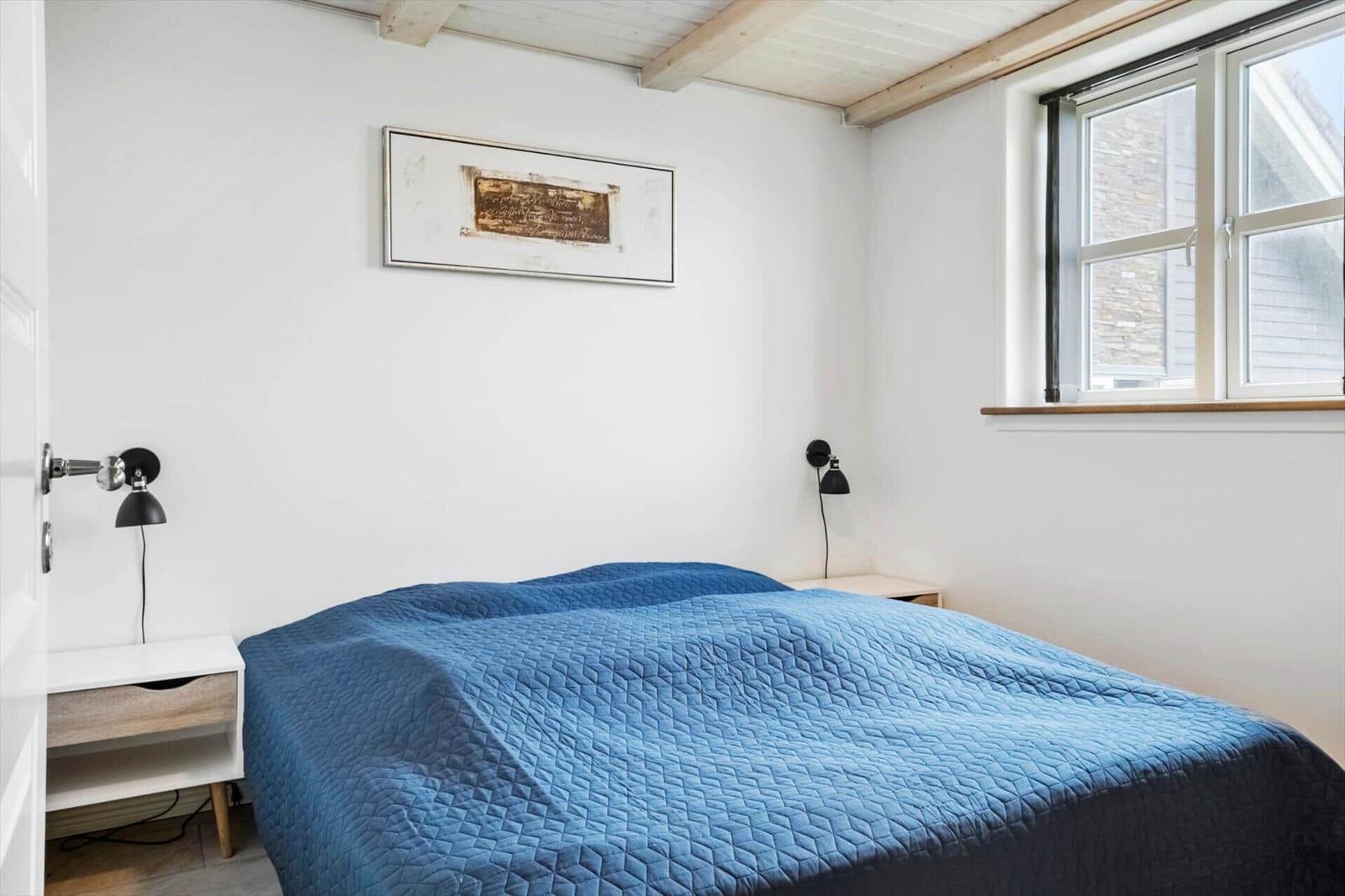 Schlafzimmer mit blauer Bettdecke, zwei Nachttischen und Wandbild.