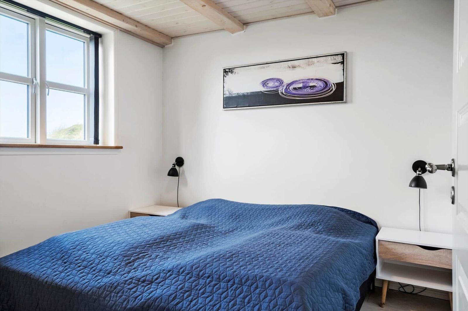 Schlafzimmer mit blauem Bett, Fenster und Wandbild.
