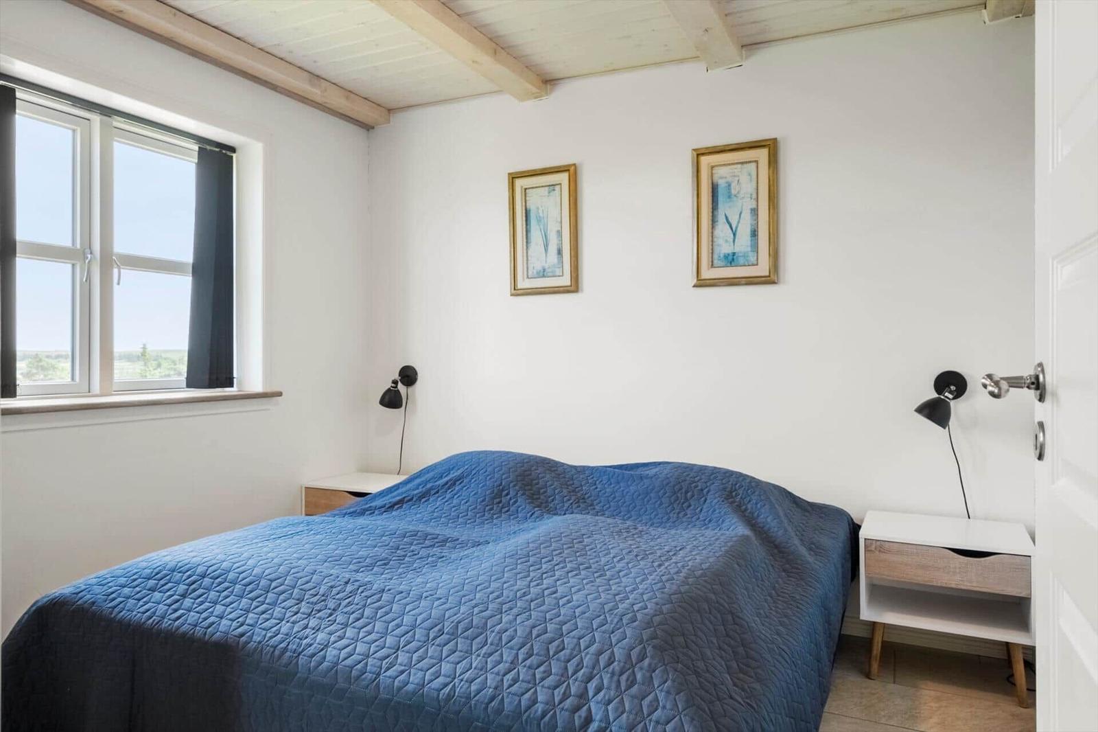 Schlafzimmer mit blauer Bettdecke, Fenster und zwei Wandlampen.