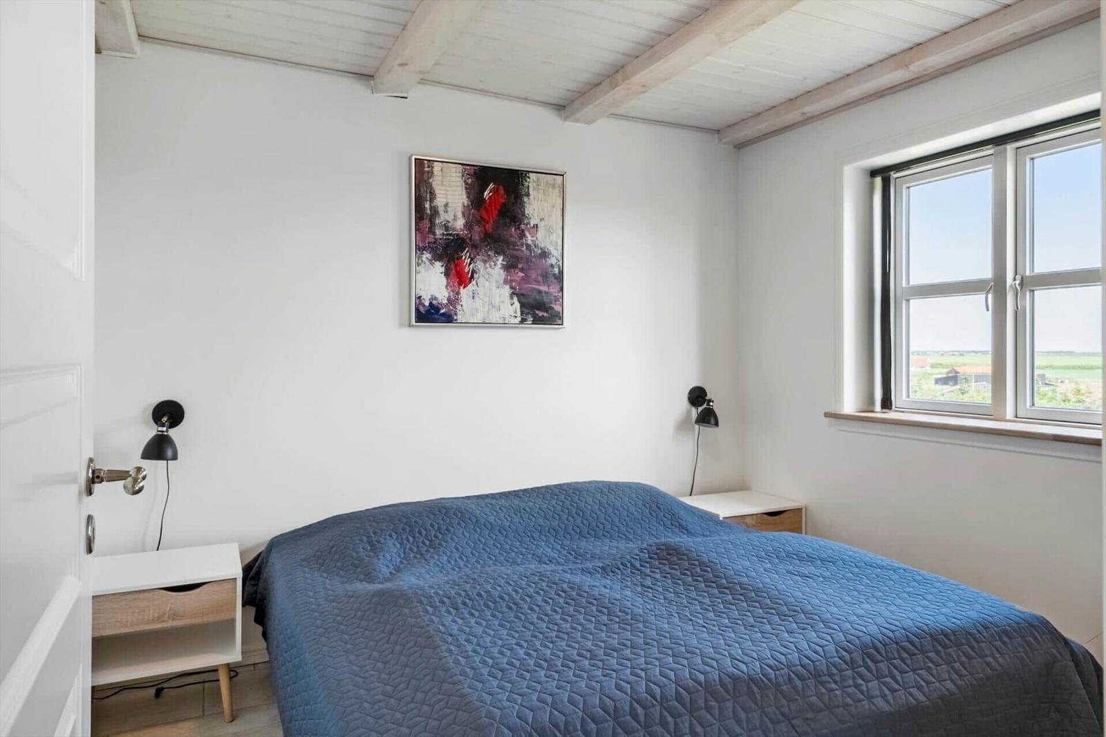 Schlafzimmer mit blauem Bett, Fensterblick und Wandbild.