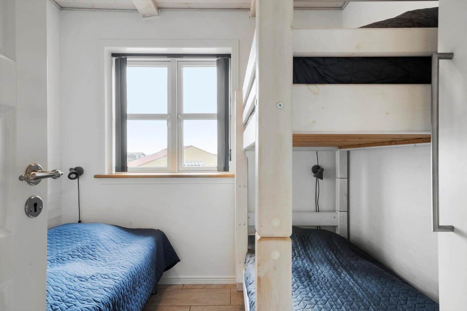 Zimmer mit Doppelstockbett und Einzelbett, Fenster mit Blick auf Dächer.