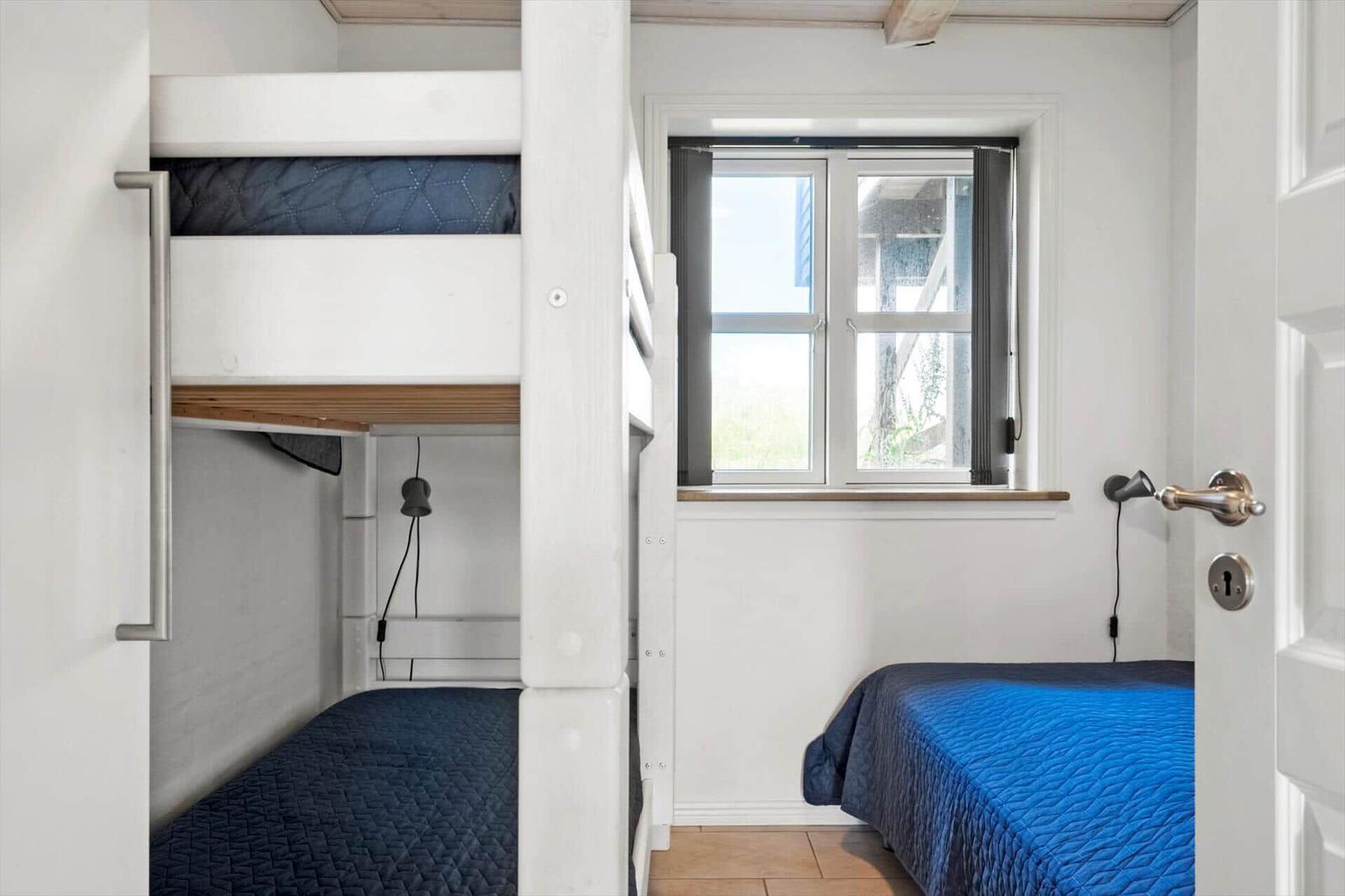 Zimmer mit Doppelbett und Kojenbett, Fenster und Tür sichtbar.