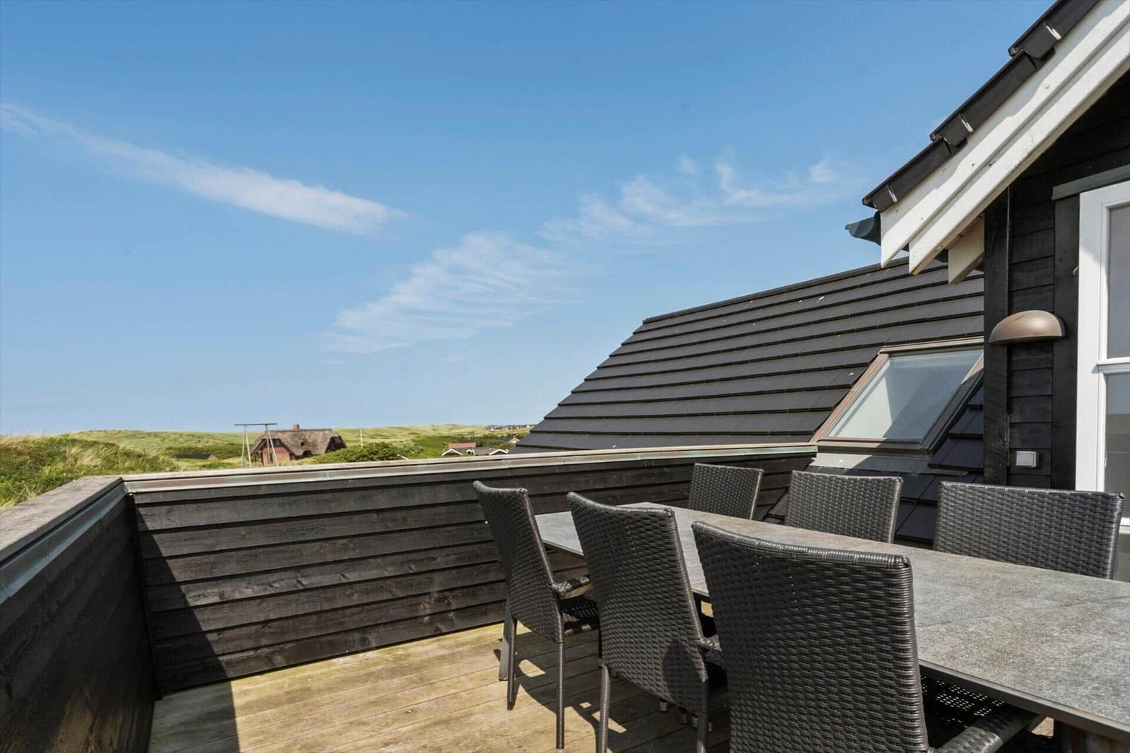 Terrasse mit Tisch und Stühlen, Blick auf grüne Hügel und Himmel.