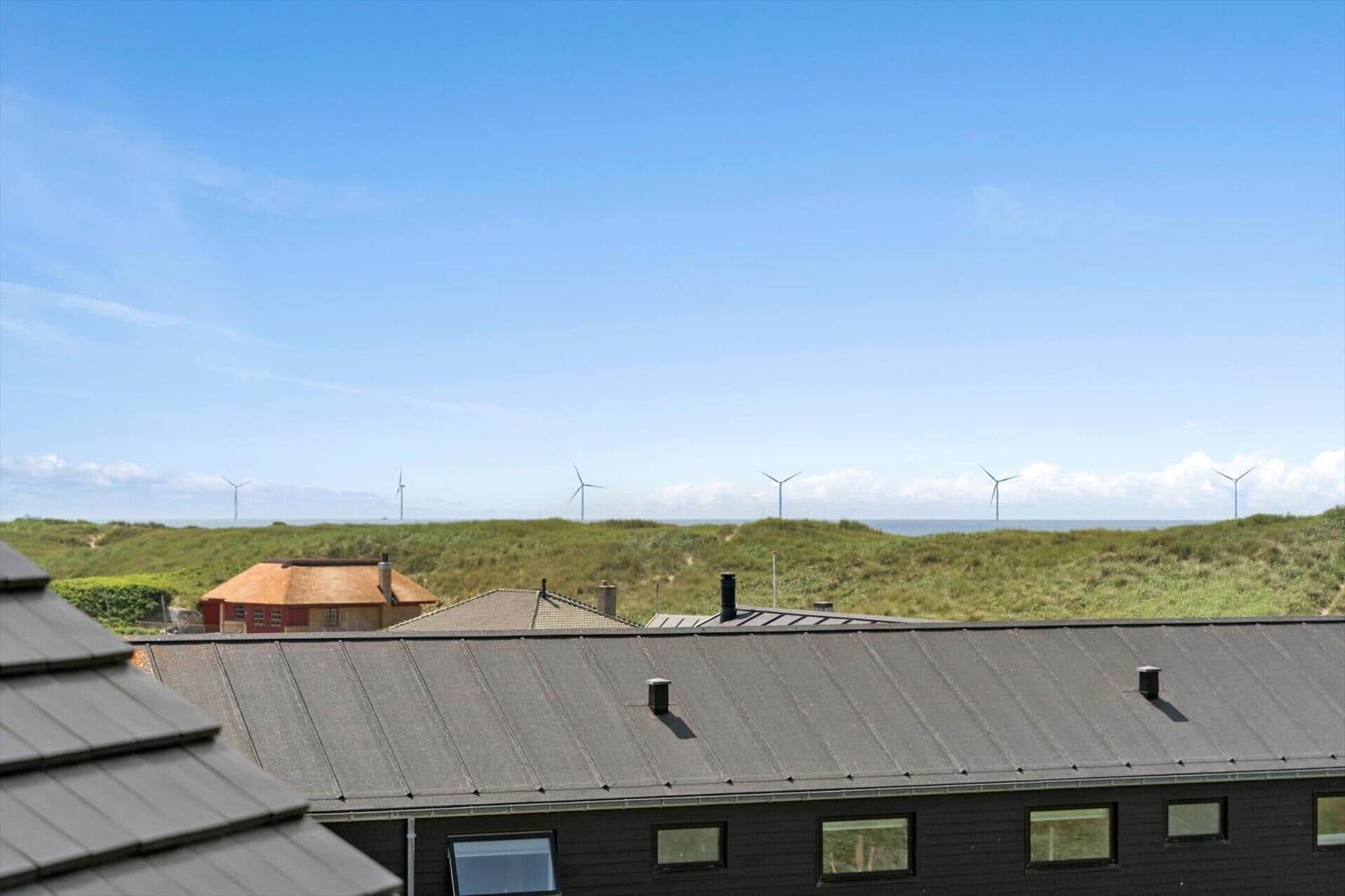 Dach mit Blick auf grüne Dünen und Windkraftanlagen am Horizont.