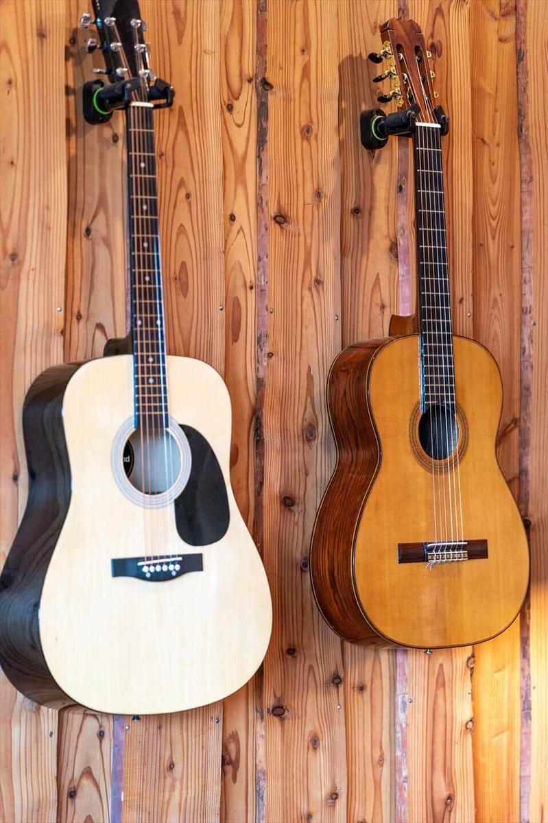 Zwei Akustikgitarren hängen an einer Holzwand.