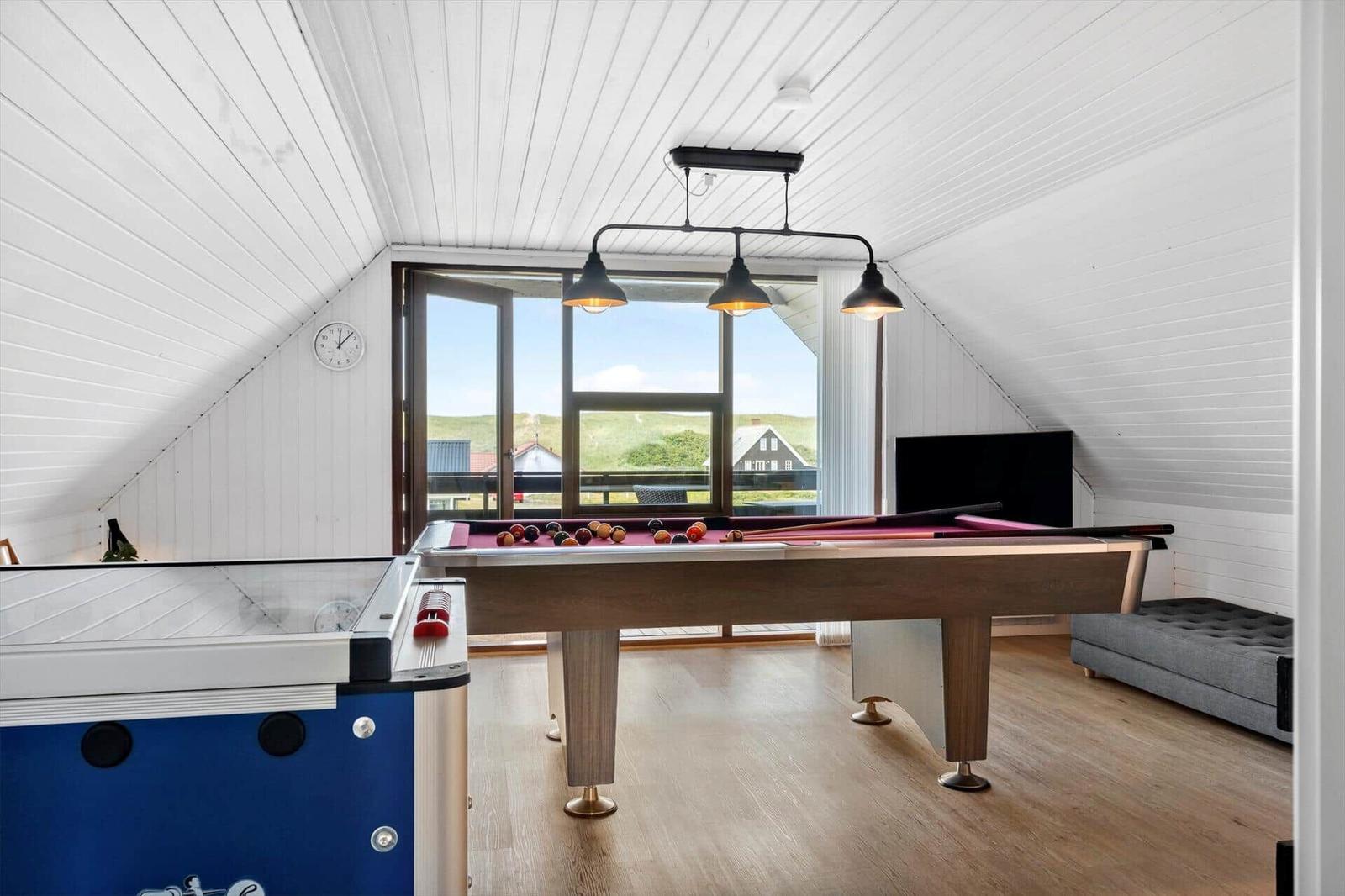 Raum mit Billardtisch, Luftbildfenster und Fernseher. Holzboden und weiße Wände.