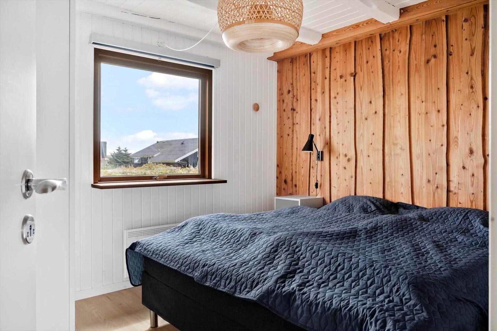 Schlafzimmer mit Holzwand, Bett und Fensterblick auf Dach