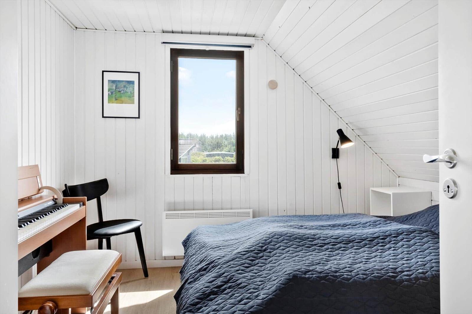 Schlafzimmer mit Bett, Klavier und Fenster mit Blick auf die Landschaft.