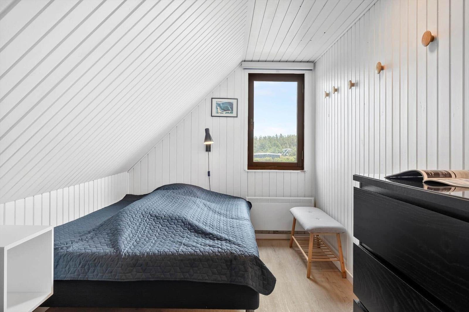 Schlafzimmer mit Dachschräge, Bett, Fenster und Schrank.