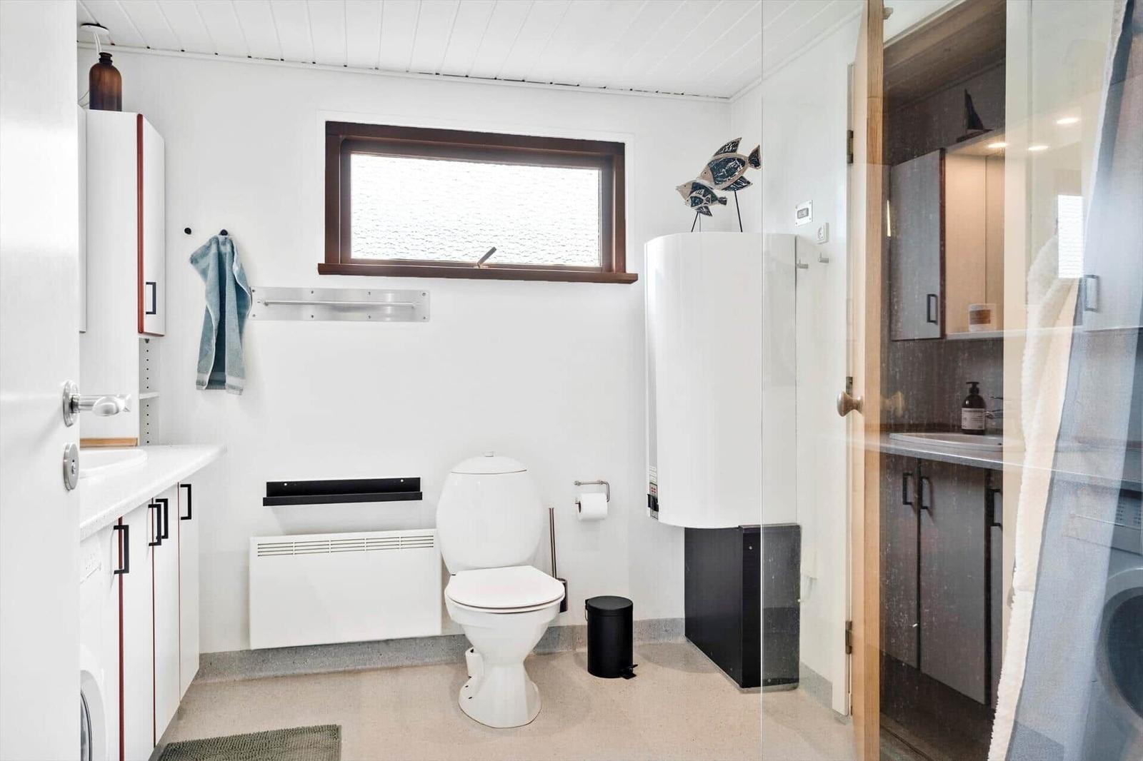 Badezimmer mit Toilette, Waschbecken und Dusche. Fenster, Heizkörper und dekorative Fische sichtbar.