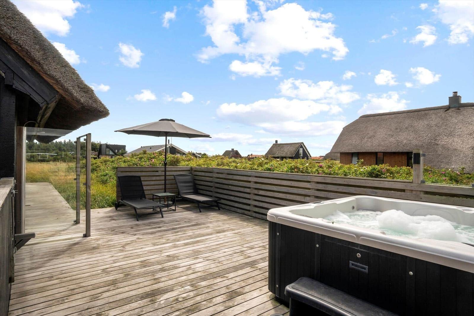 Terrasse mit Whirlpool, Sonnenliegen und Sonnenschirm. Blick auf traditionelle Häuser mit Strohdächern.