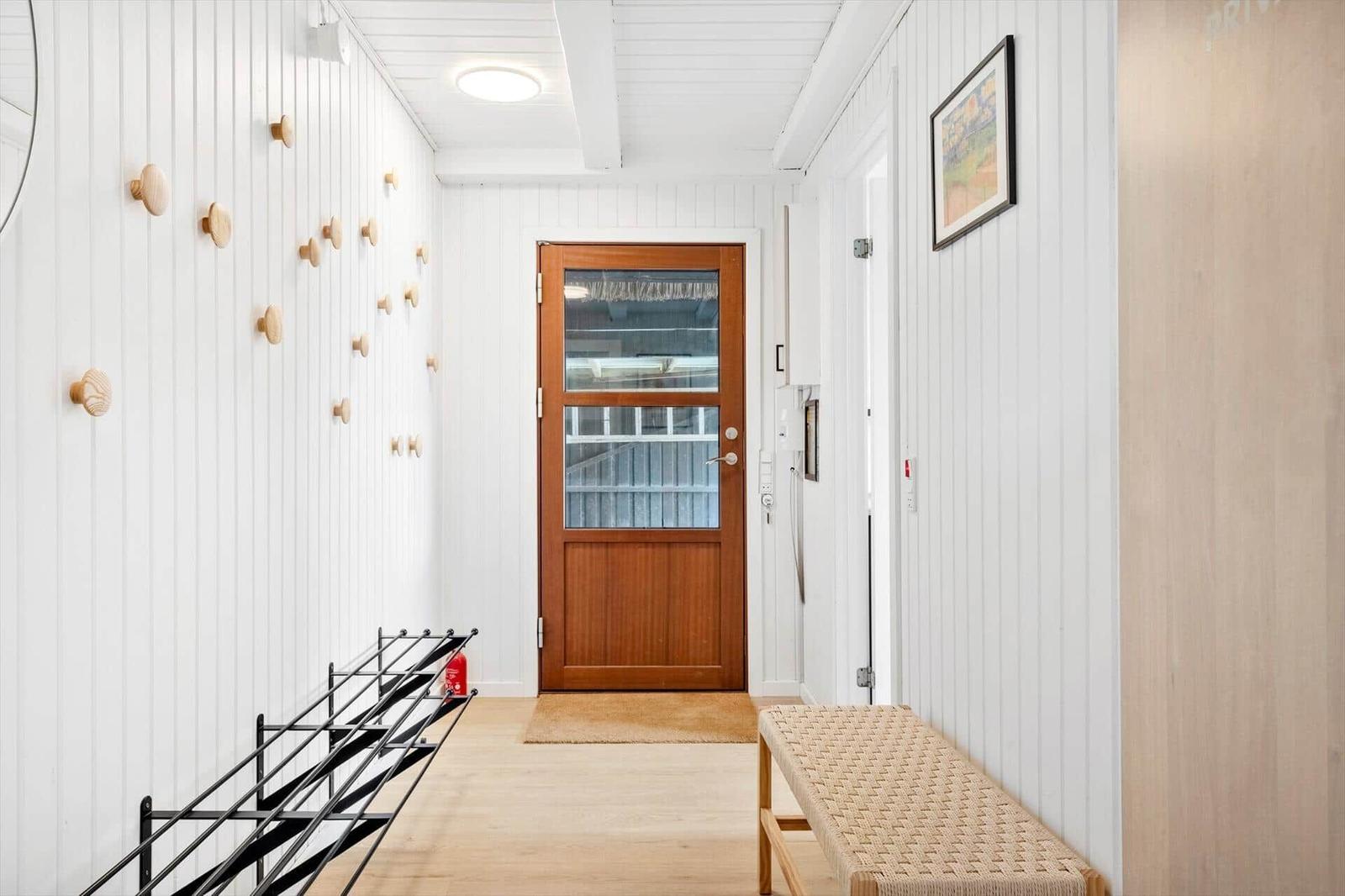 Eingangsbereich mit Holztür, Wand mit Holzknöpfen und Bänkchen.