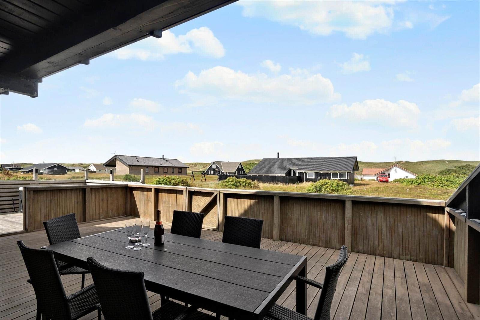 Terrasse mit Tisch und Stühlen, Blick auf Häuser und Hügel unter blauem Himmel.