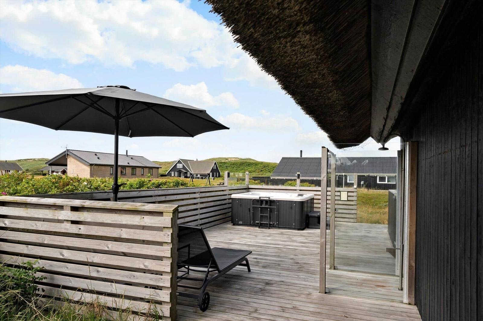 Terrasse mit Liegestuhl, Sonnenschirm und Whirlpool. Blick auf Häuser und Hügel.