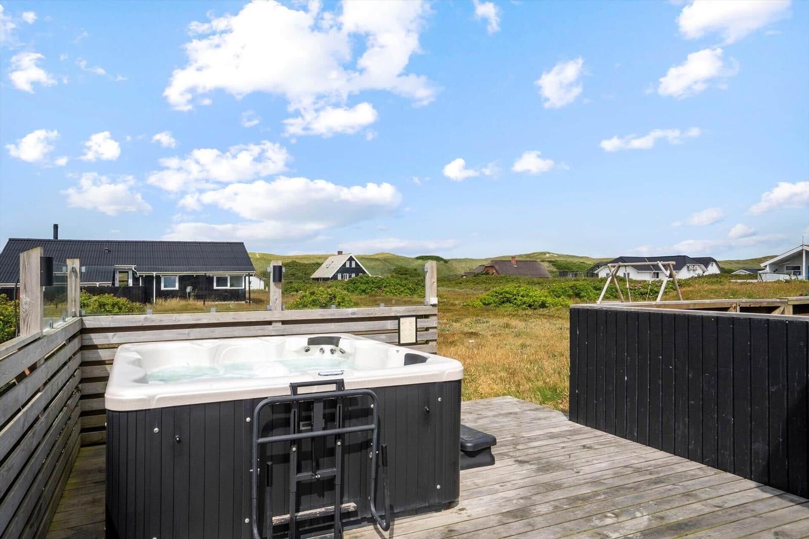 Hochwertiger Whirlpool auf Holzterrasse mit Blick auf Grünland und Häuser.