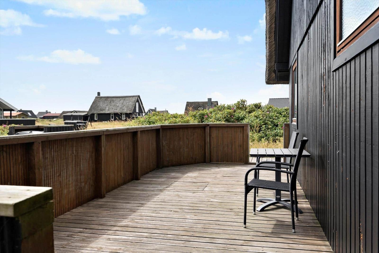 Holzterrasse mit Tisch und Stühlen, Blick auf Dächer und Grün.