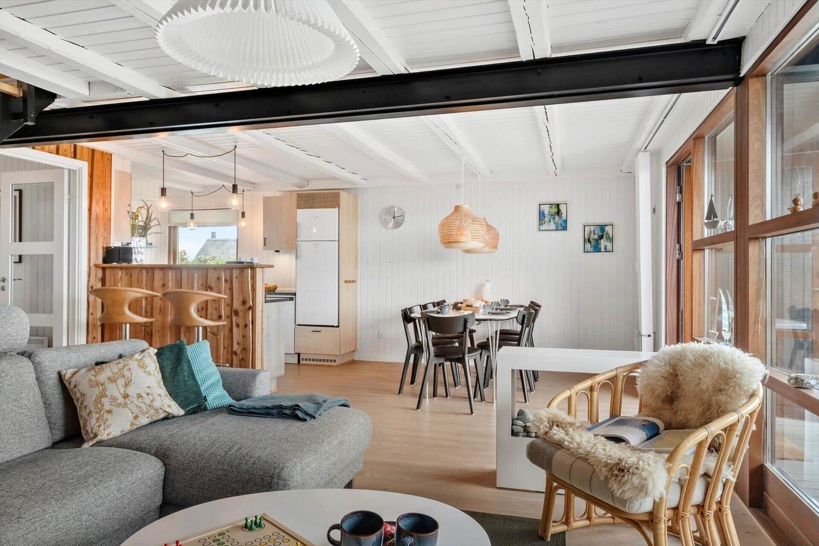 Wohn- und Essbereich mit Sofa, Esstisch und Küchenbereich. Holzboden und weiße Wände.