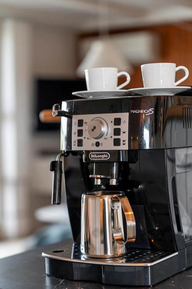 Espresso-Kaffeemaschine mit zwei Tassen und Milchkanne auf Arbeitsfläche.