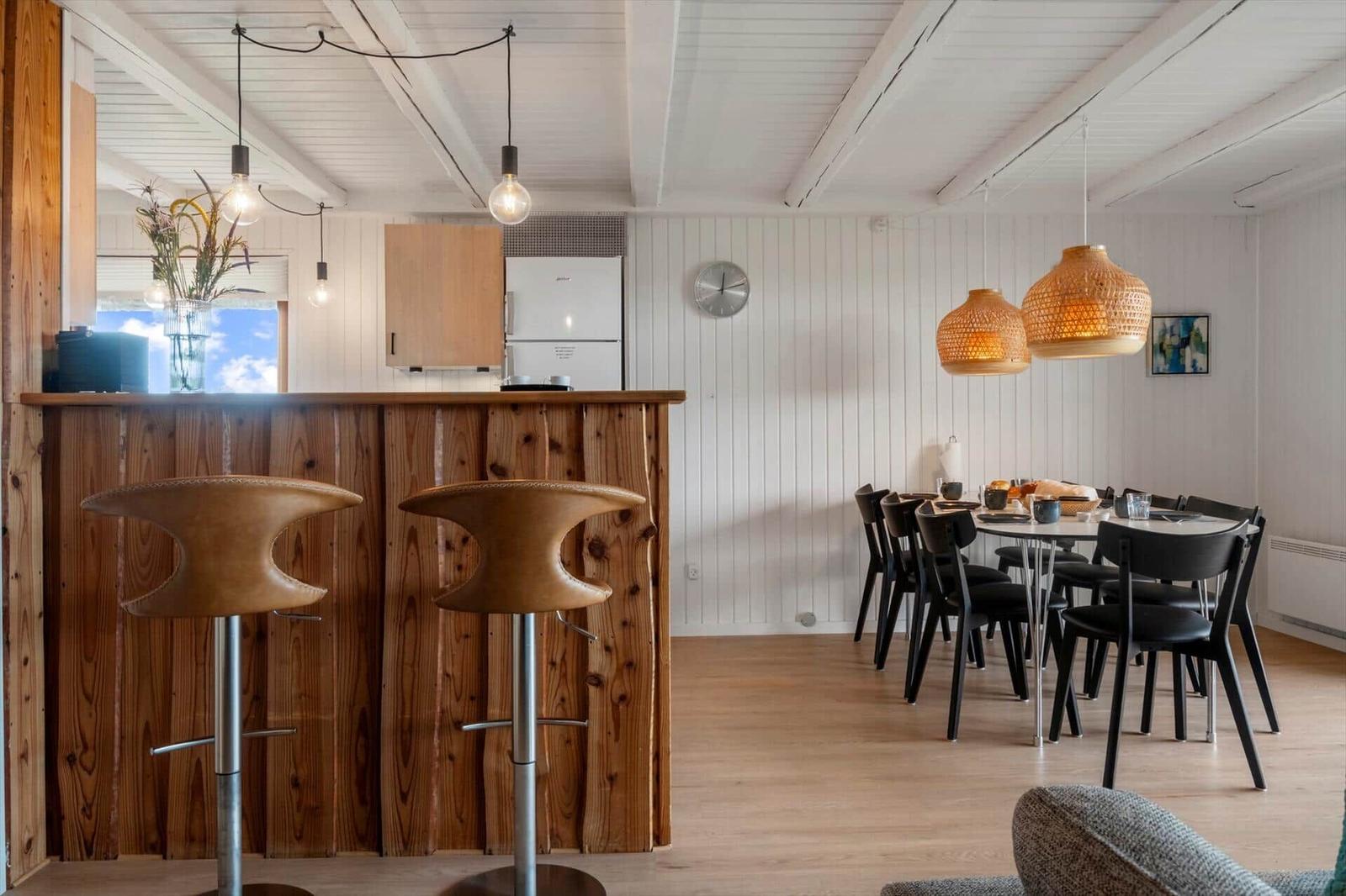 Küche mit Holzbar, Esstisch mit Stühlen und hängenden Lampen.