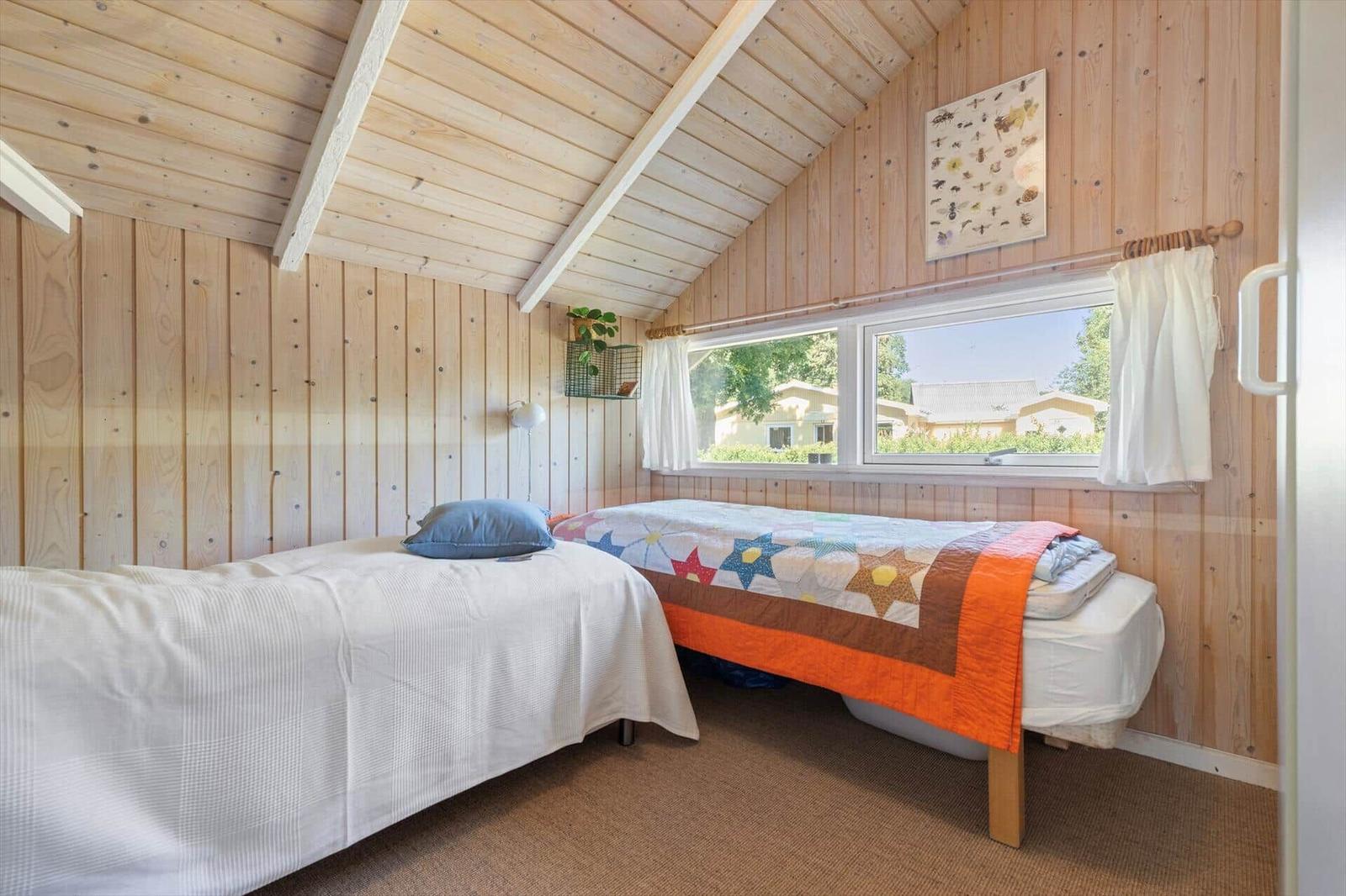 Zwei Betten in einem Holzhauszimmer mit Dachschräge und Fensterblick.