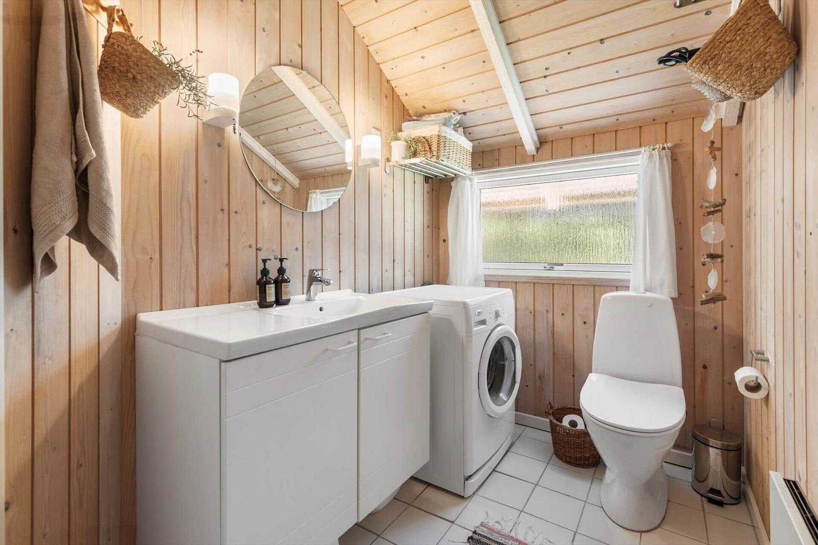 Bad mit Waschmaschine, Toilette und Spiegel an Holzwand.