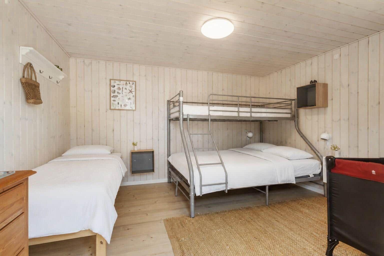 Zimmer mit Kojenbett, Einzelbett und Holzwandverkleidung.