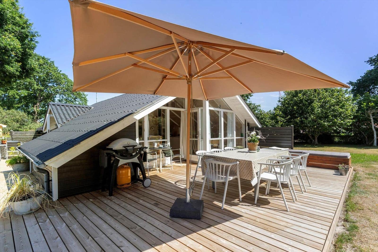 Terrasse mit Tisch, Stühlen und Sonnenschirm. Grill und Sitzbank sind vorhanden.