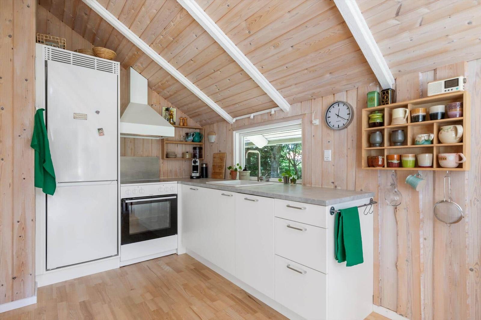 Küche mit Holzwand, weißer Küchenzeile und Kühlschrank unter Dachschrägen.