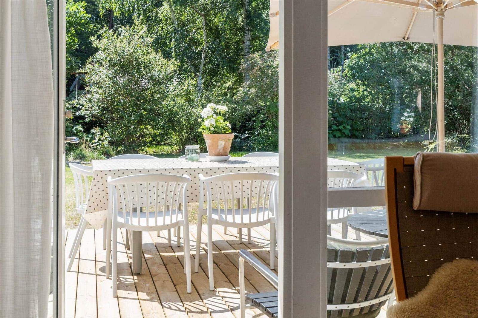 Terrasse mit Tisch, Stühlen und Sonnenschirm. Hintergrund: grüner Garten.