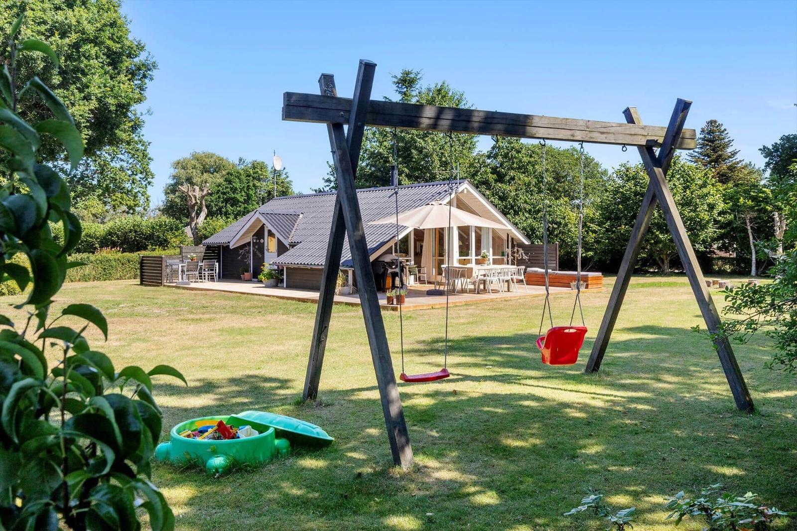 Haus mit Garten, Schaukel und Spielplatz. Terrasse mit Tischen und Stühlen.