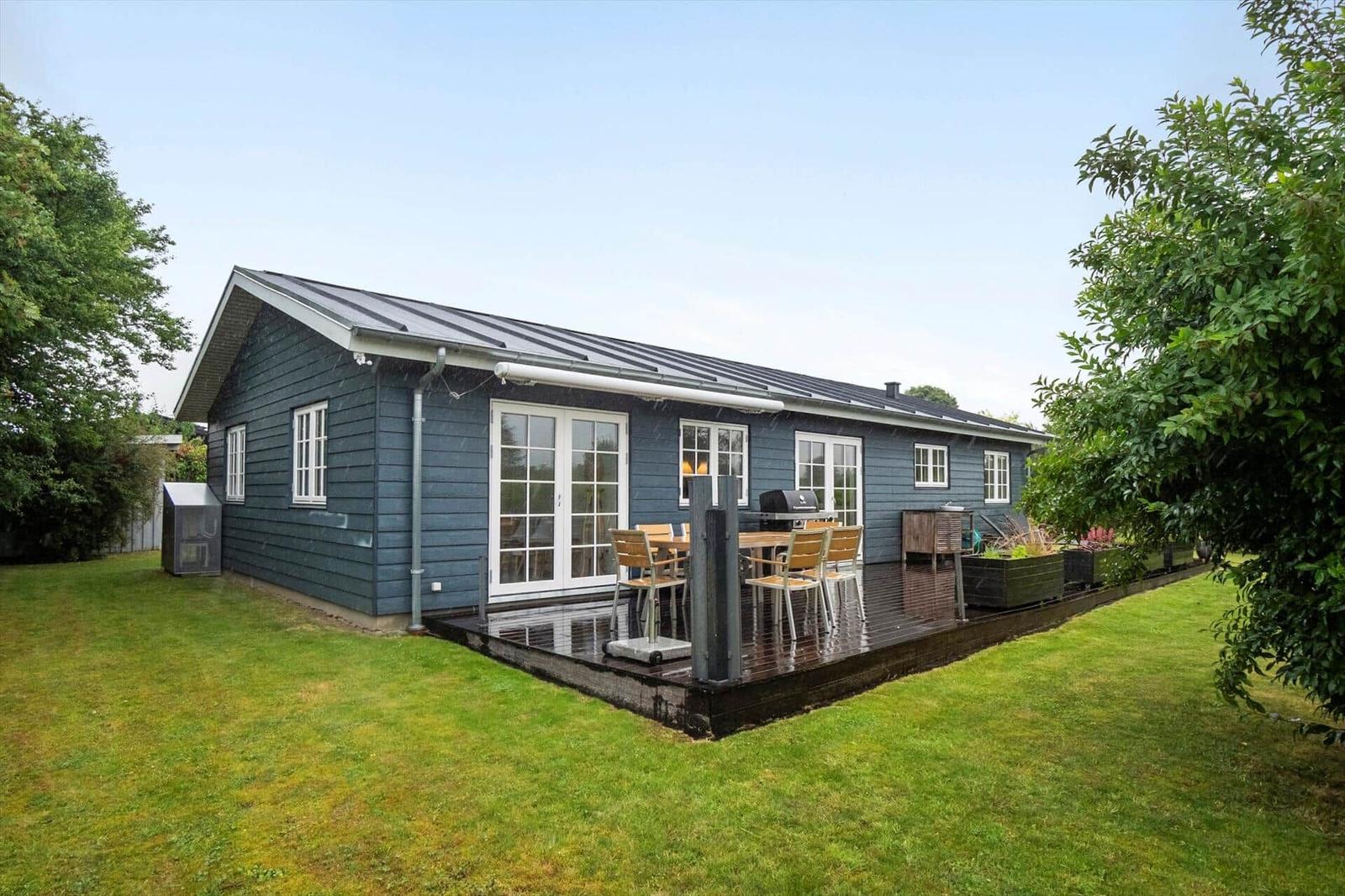 A blue house with a terrace, grill, and garden. White windows and doors.