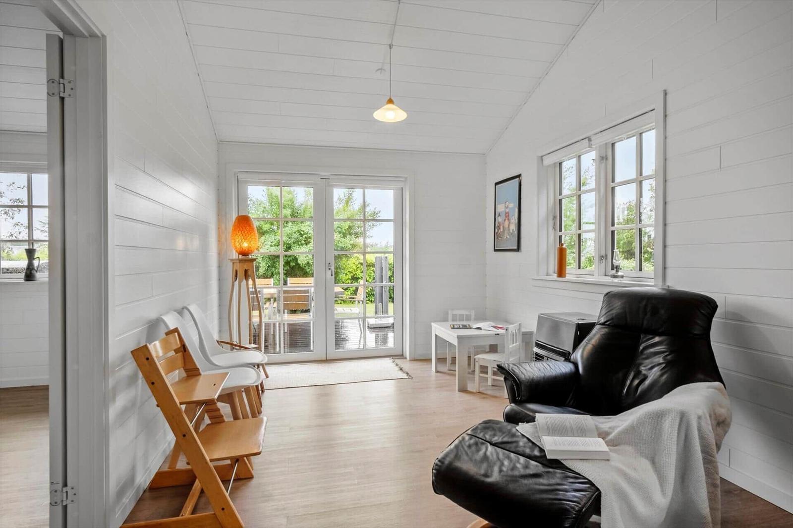 A room with white walls, a black chair, and a table. Through glass doors, a garden is visible.