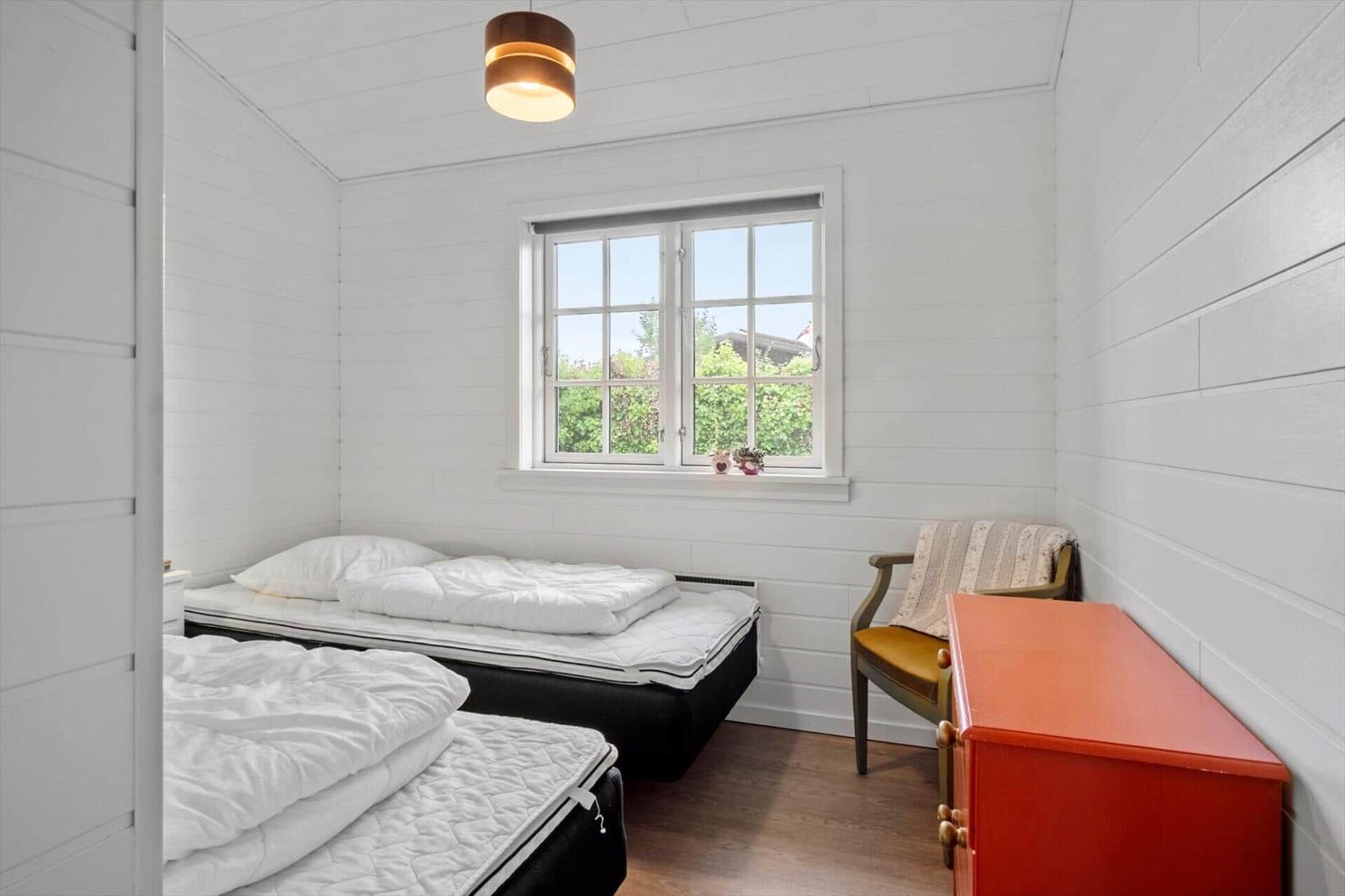 Room with two beds, window and chair. Wooden walls and ceiling.